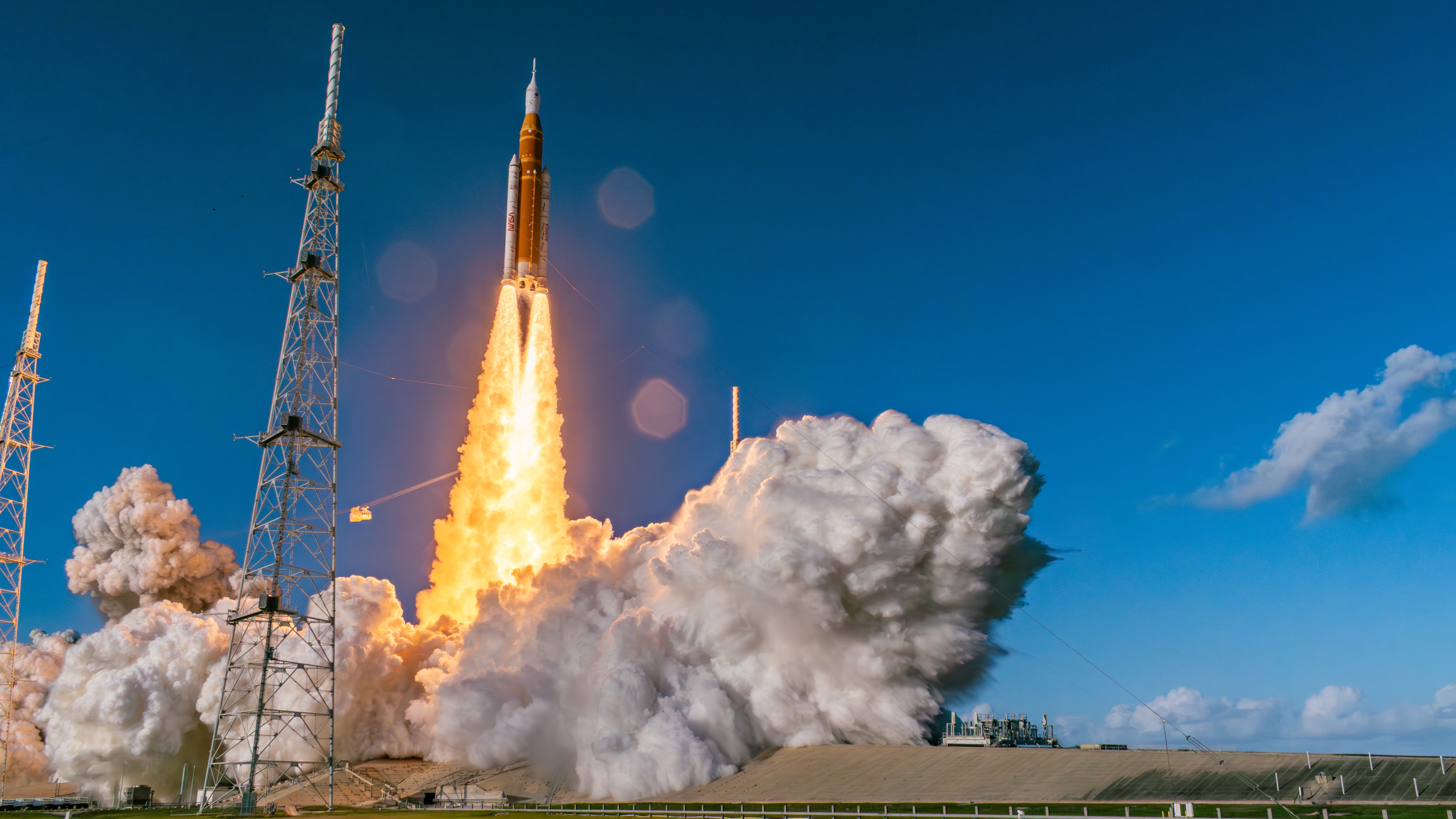 An orange rocket with two white side boosters blasts off into a blue sky.
