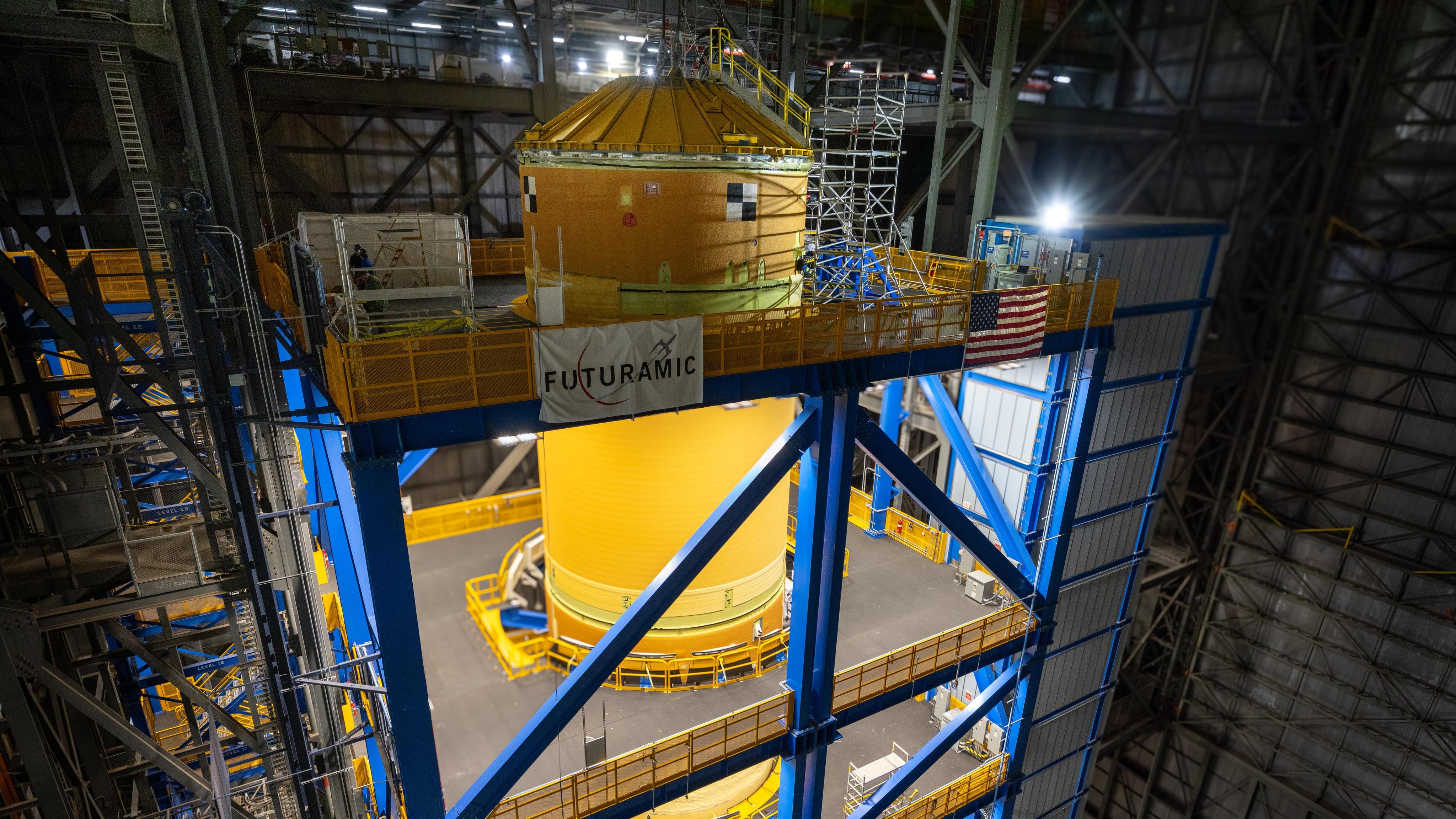 A big orange fuel tank stands vertical surrounded by scaffolding 
