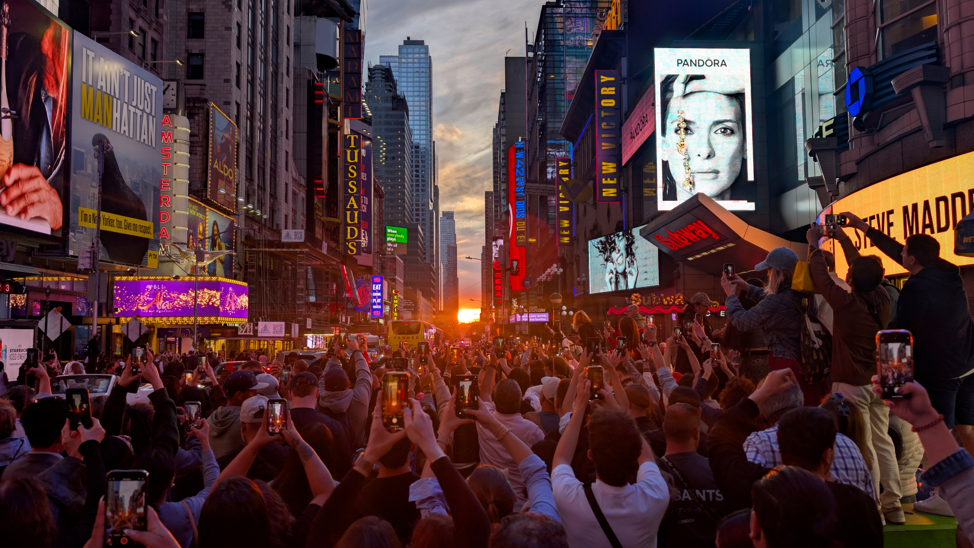 people taking photos of manhattanhenge with the sun setting lining up with the street