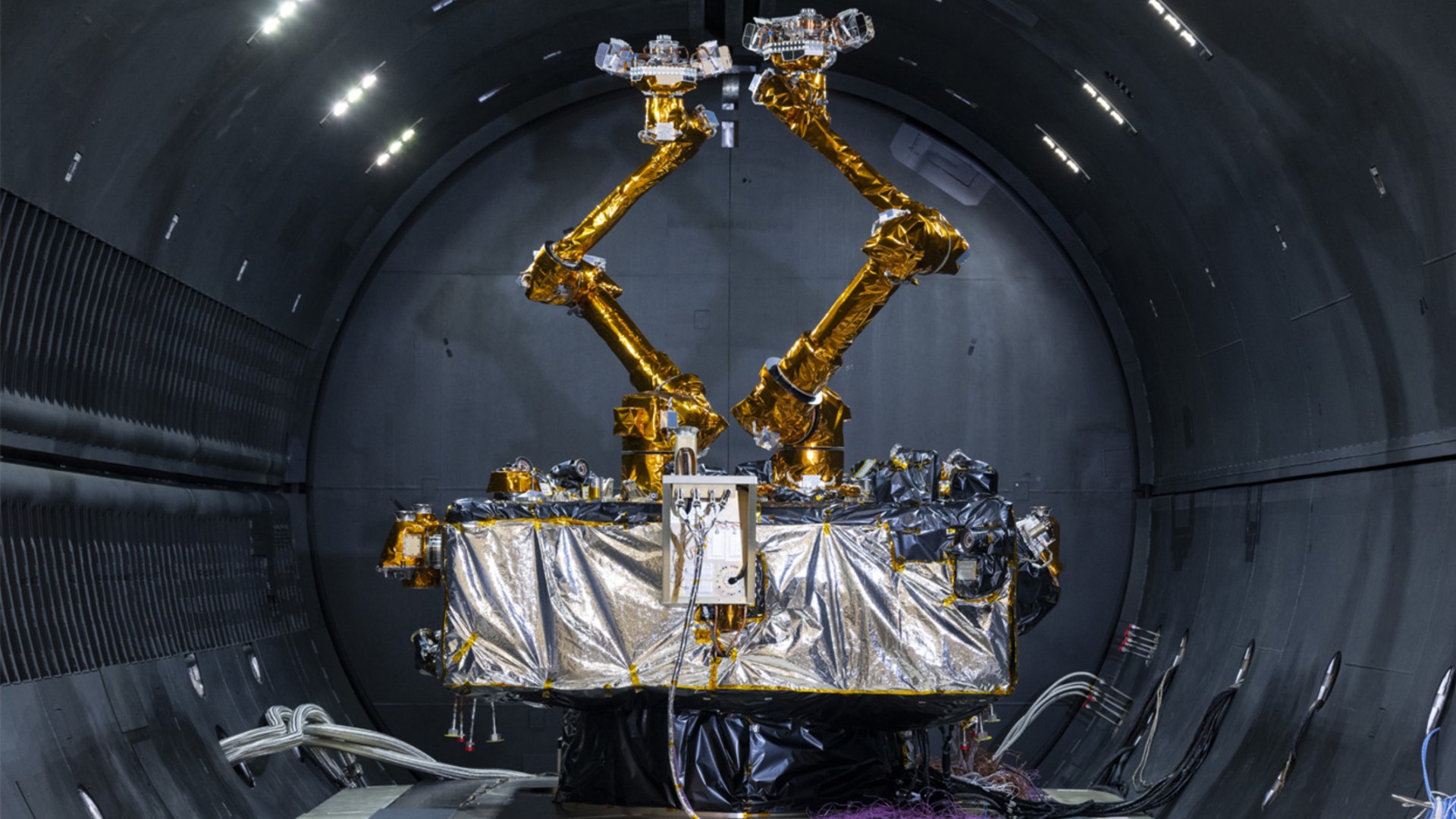 a cube-shaped satellite with two multi-jointed arms inside a cleanroom