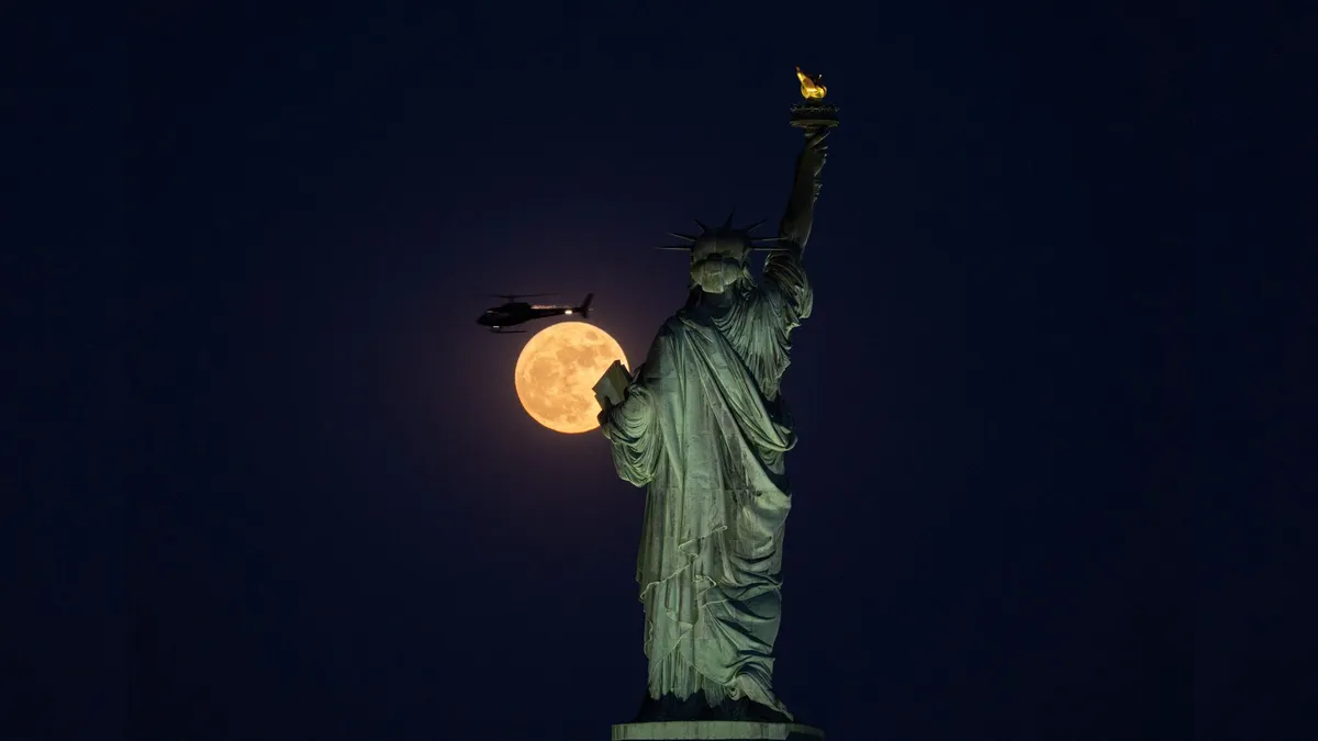 A helicopter passes in front of the near-full moon behind the Statue of Liberty. Photo by Lokman Vural Elibol/Anadolu via Getty Images